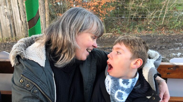 A smiling mum and her sitting on a bench, looking at each other with joy.