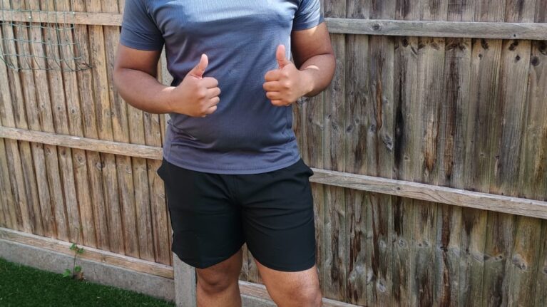 A man is smiling at the camera with his thumbs up. He is wearing running kit and stood in his garden.