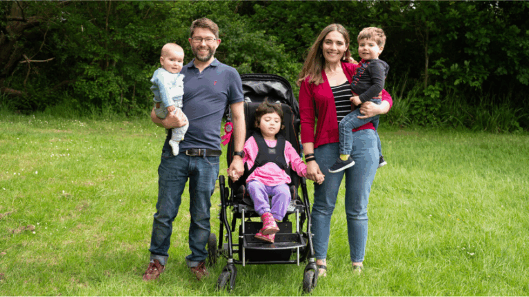 From left to right: Leia's dad holding her baby brother, Leia in a buggy, Leia's mum holding her other brother