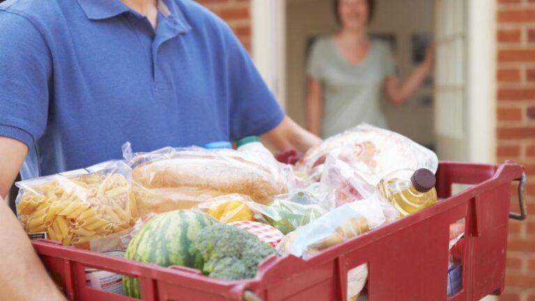Man in blue t-shirt holding a box of food at someone's front door