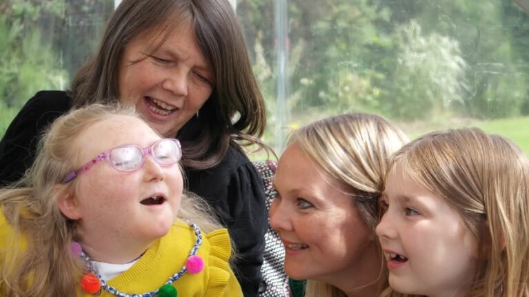 A family of two women and a young girl are smiling at another family member, a young girl